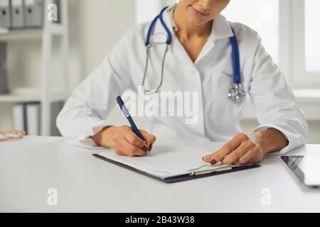 La donna medico senza volto scrive una prescrizione negli appunti mentre si trova in ufficio clinica. Foto Stock