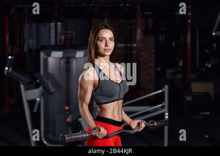 Giovane bella sportswoman fare esercizi in palestra con un barbell. Contesto di concetto di idoneità. Foto Stock