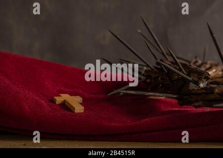 Primo piano di una piccola croce di legno e di una rappresentazione della corona di spine di Gesù Cristo su un panno rosso su una superficie di legno Foto Stock