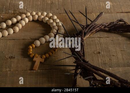 Concetto di passione, crocifissione e resurrezione. Simboli iconici relativi alla Domenica delle Palme e al riposo di Pasqua su un tavolo di legno, corona di spine e un rosario Foto Stock