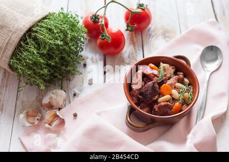 Cassoulet. Contenente salsicce di carne di maiale, oca, anatra e talvolta montone e due tipi di fagioli bianchi. Cucina francese. Su vecchia ba bianca di legno Foto Stock