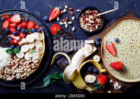 Panello indonesiano dolce martabak manis o téang bulan con gocce di cioccolato, arachidi, fragole, mirtilli, banana, formaggio, su sfondo scuro Foto Stock