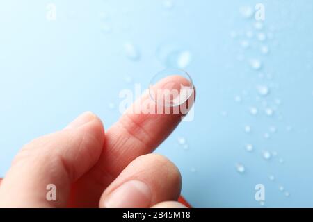 La mano femmina tiene la lente a contatto su sfondo blu, primo piano Foto Stock