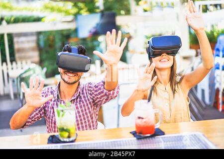 Amici stupiti guardando in VR occhiali e gesturing con le mani in cocktail bar ristorante - giovani divertirsi con nuove tendenze del telefono - tecnologia Foto Stock