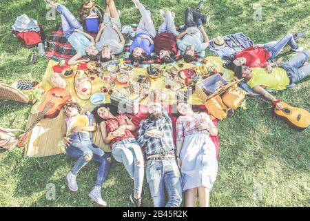 Amici felici sdraiati al picnic con barbecue sul parco della città all'aperto - giovani che mangiano insieme nel tempo estivo - Focus sul bordo inferiore GU Foto Stock