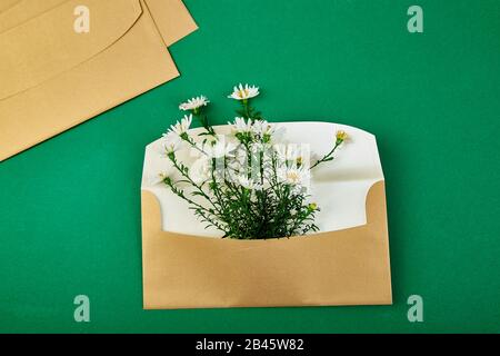 Busta in oro con una molla floreale su sfondo verde. Appartamento laico, vista dall'alto. Aperta la busta. Messaggio di saluto festivo concept Foto Stock