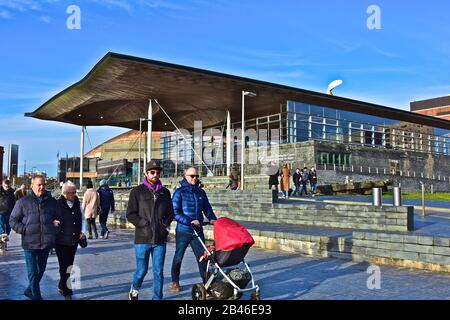 Persone che passeggiano davanti al Senedd, conosciuto anche come l'Assemblea Nazionale per il Galles, nella zona della Baia di Cardiff della città. Foto Stock