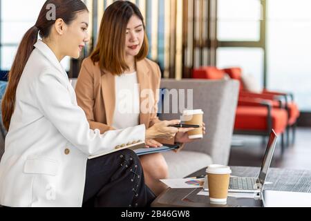 Due donne d'affari asiatiche che lavorano con il commercio del socio dalla penna del punto al laptop di tecnologia nell'ufficio moderno o nello spazio di coworking, pausa del caffè, partn Foto Stock