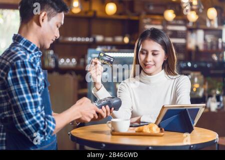 Cliente asiatico donna che paga con carta di credito via tecnologia senza contatto nfs al proprietario asiatico Small Coffee shop al tavolo femminile in caffetteria, Small busine Foto Stock