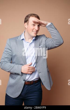 Ritratto di bell'uomo in grrey e vestito blu ufficio guarda in lontananza e sorride Foto Stock