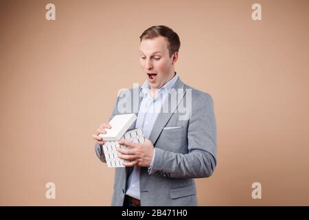 Ritratto di bell'uomo in grrey e blu vestito da ufficio tiene una scatola bianca ed è sorpreso Foto Stock
