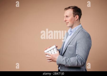Ritratto di bell'uomo in grrey e blu vestito da ufficio tiene una scatola bianca ed è sorpreso Foto Stock