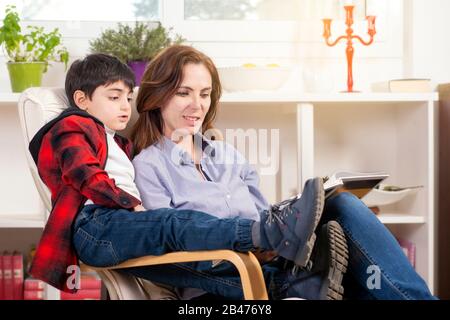 la madre legge un libro di storia al suo bambino ditting nel suo soggiorno Foto Stock