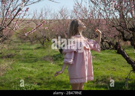 Bella donna bionda in abito rosa cammina attraverso il giardino fiorito Foto Stock