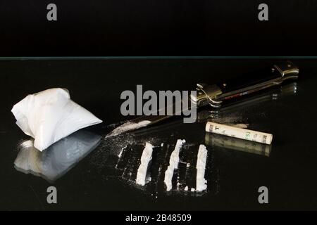 Un sacco e linee di cocaina. Una switchblade e la banconota arrotolata sul tavolo. Parte della lama di rasoio dietro la fattura. Tavolo in vetro nero. Consumo di cocaina sul coltello. Foto Stock