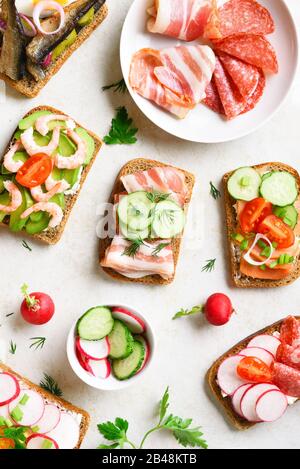 Diversi sandwich con carne, verdure, pesce. Assortimento di sandwich aperti su sfondo di pietra chiara. Gustoso spuntino sano. Vista dall'alto, piatto. Foto Stock