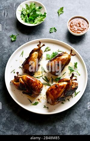 Quaglie arrosto su piastra bianca. Gustose grigliate di quaglie carcasse sulla pietra blu sullo sfondo. Foto Stock