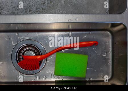 Una spazzola di lavaggio rossa e una spugna verde in un lavello in acciaio inossidabile bagnato Foto Stock