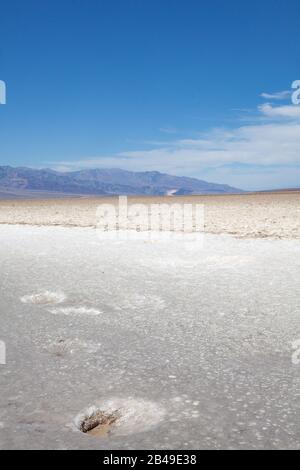 Bacino del Badwater nel Parco Nazionale della Valle Della Morte, con un buco naturale in primo piano, lago naturale di sale risultato della desertificazione del pianeta Foto Stock