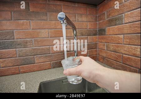 Versare l'acqua nel bicchiere dal rubinetto. Tema acqua potabile Foto Stock