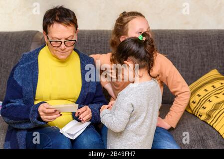 Nonna Guardando Le Vecchie Foto Con I Nipoti Per Aggiornare La Memoria. Felice Famiglia, Accogliente Home Momenti. Foto Stock