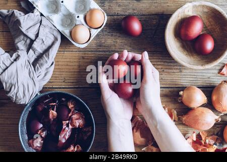 Donna che fa tinto uova di Pasqua dipinte con cipolla colorante naturale su sfondo di legno. Processo di tintura delle uova con vernici naturali per Pasqua. ecol naturale Foto Stock