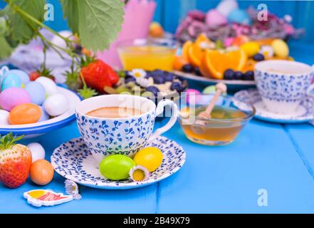 Colazione di Pasqua. Caffè espresso fresco aromatico, succo d'arancia, uova di pasqua, muesli, miele su sfondo blu di legno. Spazio di copia Foto Stock