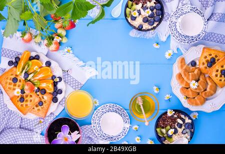 La scena della colazione di Pasqua è ripresa dall'alto. Tazze per tè, torta con marmellata, biscotti, succo d'arancia fresco, frutta, granola con frutti di bosco, miele, fragole con foglie e frutti di bosco sul tavolo Foto Stock