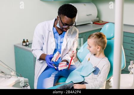 Il bambino sulla sedia del dentista che si diverte mentre si sfrega i denti con un medico africano Americano maschio. Foto Stock