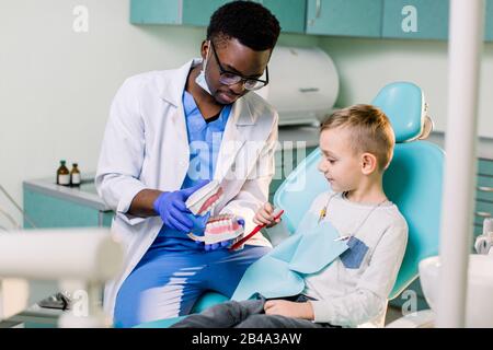 Il bambino sulla sedia del dentista che si diverte mentre si sfrega i denti con un medico africano Americano maschio. Foto Stock