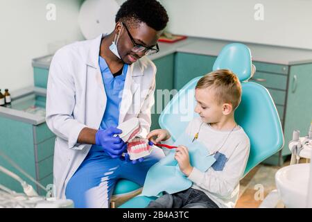 Il bambino sulla sedia del dentista che si diverte mentre si sfrega i denti con un medico africano Americano maschio. Foto Stock