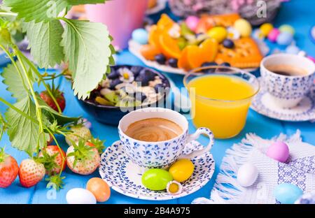 Colazione di Pasqua. Caffè espresso fresco aromatico e uova di colore pasquale su sfondo di legno blu. Muesli, fragole per colazione. Foto Stock