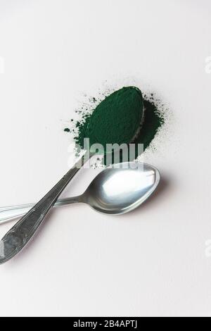 Cucchiai di metallo con polvere di spirulina, superfood su sfondo bianco Foto Stock