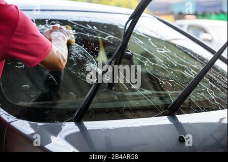 Uomo lavoratore lavaggio e sfregamento auto con spugna e acqua Foto Stock