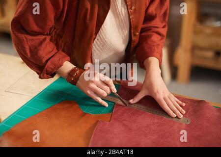 Angolo alto orizzontale primo piano di una femmina non riconoscibile artigianale che taglia il materiale in pelle Foto Stock