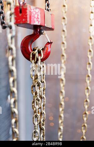maniglia a catena metallica con gancio rosso nella sala tecnica. Gancio di carico gru. Concetto di manutenzione e lavori di costruzione. Foto Stock