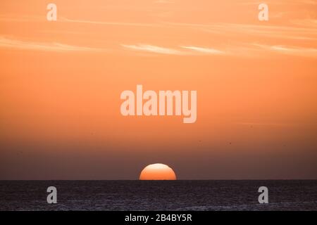 Classico tramonto tropicale o alba sul mare orizzonte con sole e acqua che si toccano insieme - arancio caldo cielo in background - destinazione viaggio paradiso concetto di vacanza Foto Stock