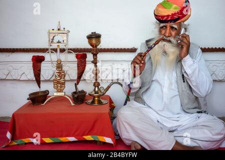 L'uomo indiano invecchiato con la barba bianca lunga e l'oppio fumante turbante colorful da un tubo dell'acqua all'interno del forte di Mehrangarh, Jodhpur, Rajasthan, India. Questo è o Foto Stock