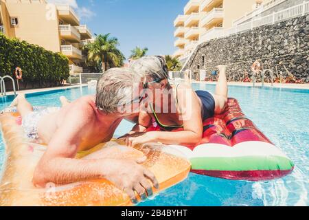 Relazione per anziani maturi anziani coppia adulti baciare in piscina divertirsi con lilo alla moda insieme in un giorno soleggiato di vacanza estiva in hotel Foto Stock