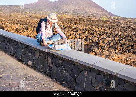 Giovane donna solitaria viaggiatore selvaggio seduto e guardando la mappa per il viaggio in aereo con deserto e montagne in background - godendo diverso concetto di vacanza per nomade Foto Stock