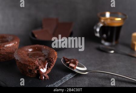 Torta di lava al cioccolato fatta in casa su un piatto nero con un caffè su sfondo nero Foto Stock