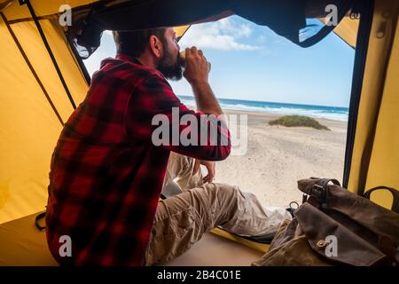 Viaggio e alternativa camera hotel concetto di destinazione con persone sole uomo bere un caffè all'interno di una tenda in campeggio libero alla spiaggia per vacanza stile di vita diverso - godendo di libertà e oceano Foto Stock