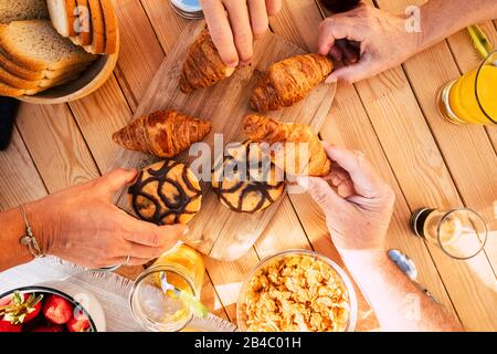 Gruppo di amici la gente della famiglia ha visto dalla vista verticale dall'alto prendere croissant e cibo misto per colazione attività mattutina - tavolo di legno in background e mani prendere per mangiare Foto Stock