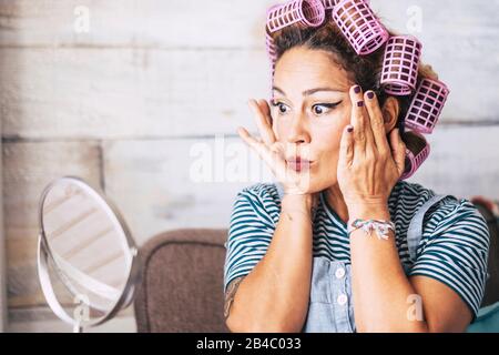 Bella e divertente espressione caucasica adulto donna che si prepara a casa di fronte allo specchio con trucco sul viso - rughe di controllo e ottenere il concetto più vecchio per i giovani - ricci sui capelli Foto Stock