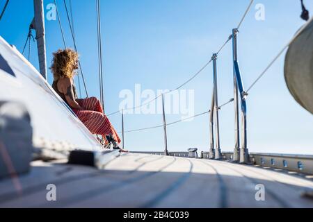 Bella curly adulto giovane donna sedersi sul molo di una barca a vela godendo il sole durante le vacanze estive vacanza tour - donna di viaggio godendo libertà e stile di vita lussureggiante in attività ricreative all'aperto Foto Stock