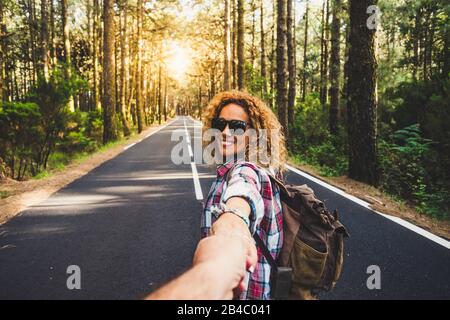 Coppie viaggiatori uomo e donna seguono le mani di tenuta a lungo strada foresta paesaggio e sole sullo sfondo Amore e Viaggi emozioni felici stile di vita concetto. Persone che viaggiano avventure attive vacanze