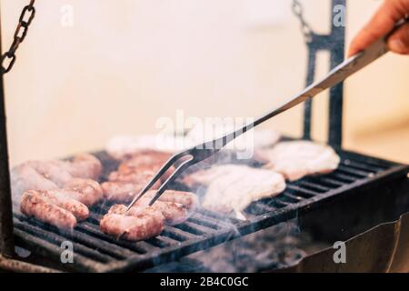 Primo piano di carne di cucina chef su una griglia calda - salsicce su barbecue - casa nbarbecue per condividere la cena con gli amici in attività ricreative all'aperto per il festivio o concetto di vacanza Foto Stock