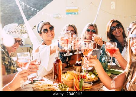 Allegro gruppo di felici donne che si sono messe in sedia e si sono arrostite con amicizia e felicità - giovani e adulti hanno divertimento mangiare - cibo e bevande celebrazione concetto Foto Stock