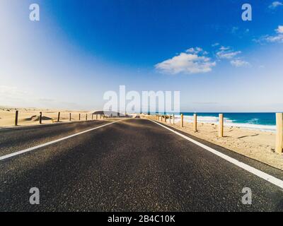 Long Way Road per il trasporto di auto da viaggio concetto con deserto e spiaggia sul lato - acqua di mare e blu chiaro cielo in background - effetto movimento Foto Stock