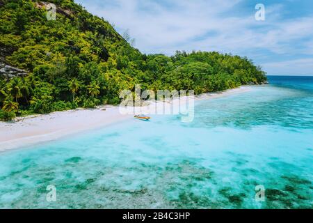 Aereo drone vista pittoresca spiaggia con palme e barca turistica solitaria in blu chiara laguna sull'isola Therese di Mahe, Seychelles. Foto Stock
